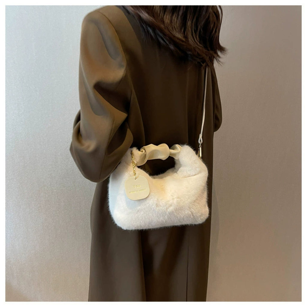Person wearing a brown coat holding a white fur handbag against a neutral background