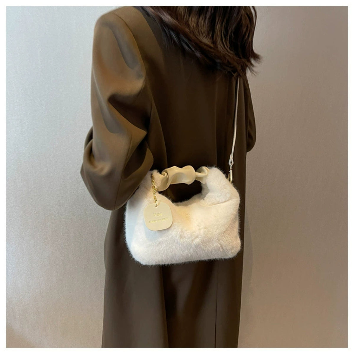 Person wearing a brown coat holding a white fur handbag against a neutral background