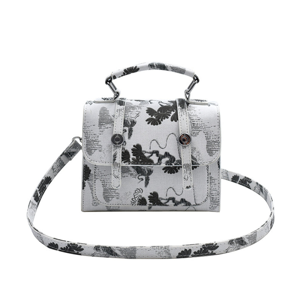 A structured sling bag and handbag with a top handle and detachable shoulder strap, featuring a black and white botanical and abstract pattern over a light gray base, shown on a plain white background.